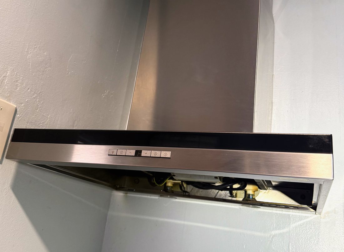 Wall-mounted stainless chimney range hood opened for service in Bergen County, NJ — filters out, blower housing and wiring exposed